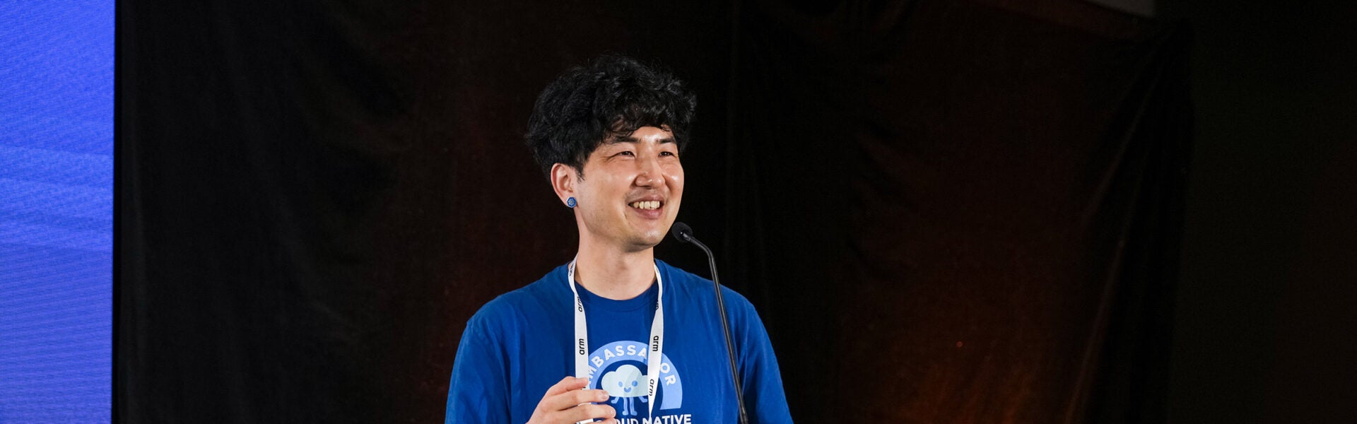 Person smiling while speaking at a conference podium with a microphone.