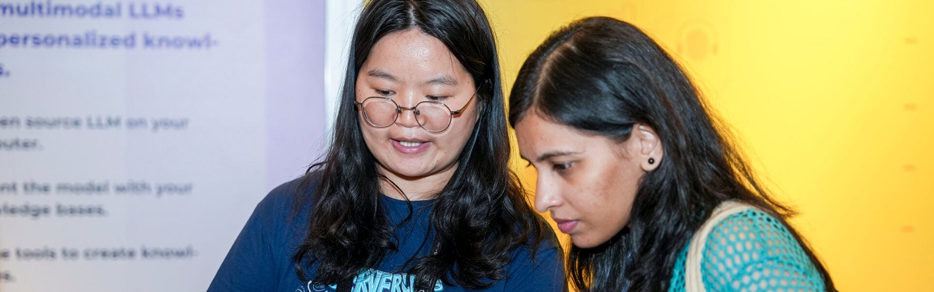 Two attendees collaborate at an exhibitor booth, reviewing information on a screen.